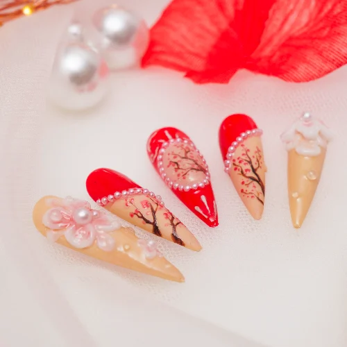 Glossy red press-on nails with peach blossom details and pearl accents